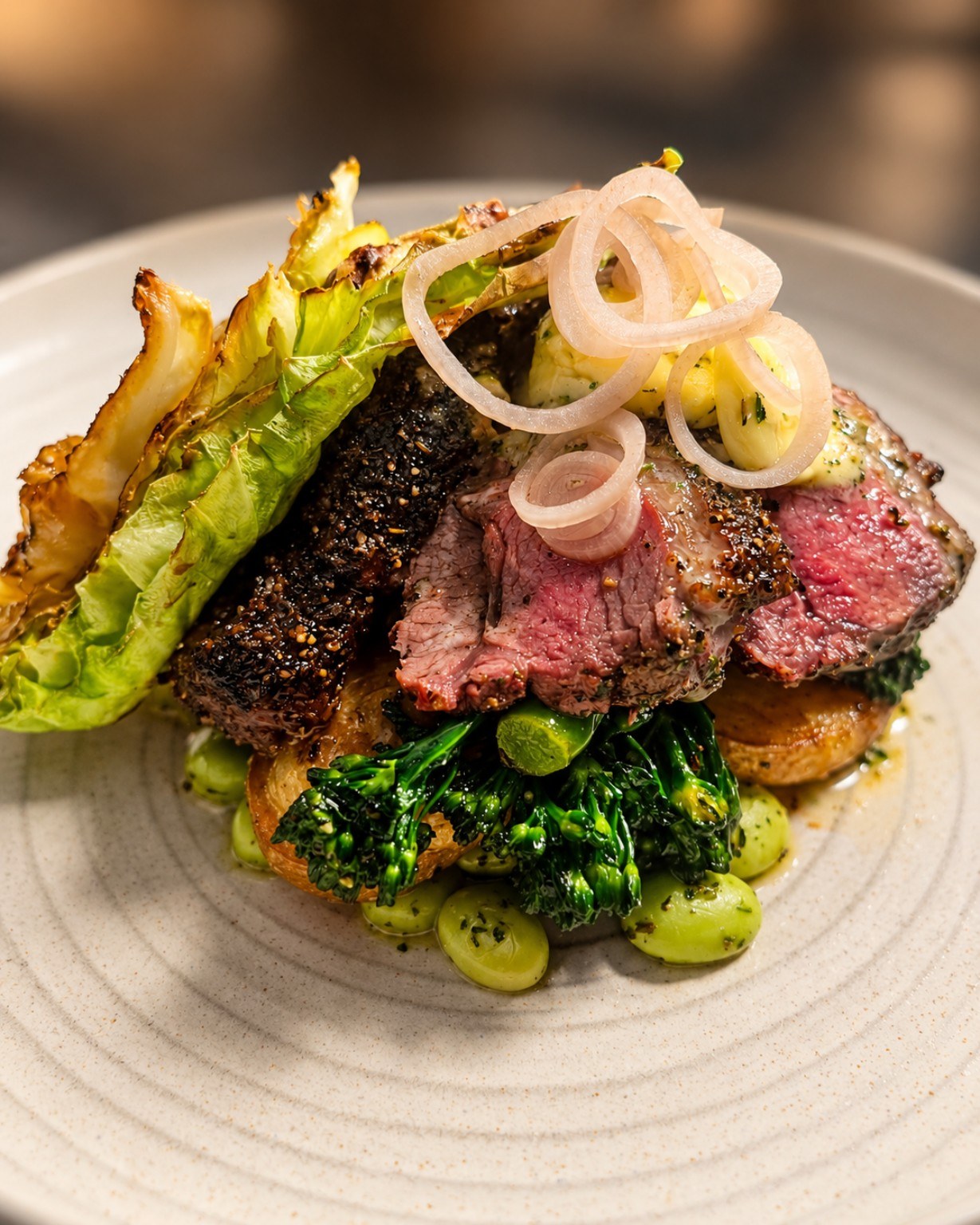 Plated lamb dish with greens and pickled onions